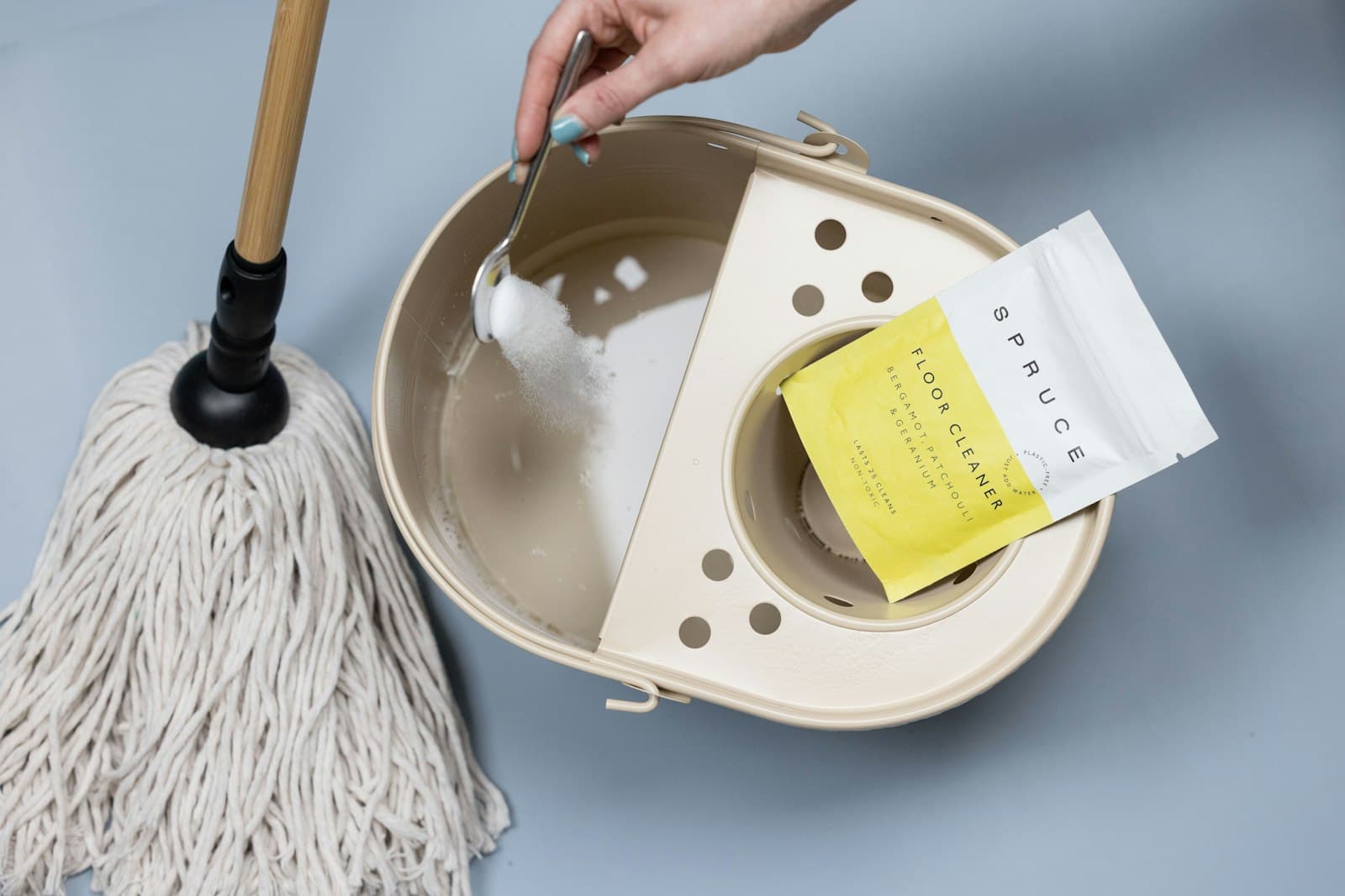 A string mop beside a bucket being filled with floor-cleaning powder
