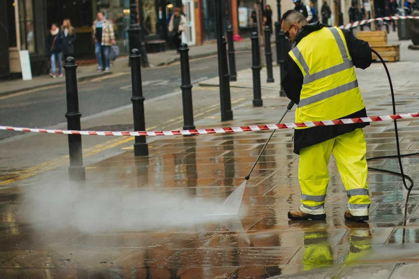 A worker in a high-visibility jacket using a pressure washer
